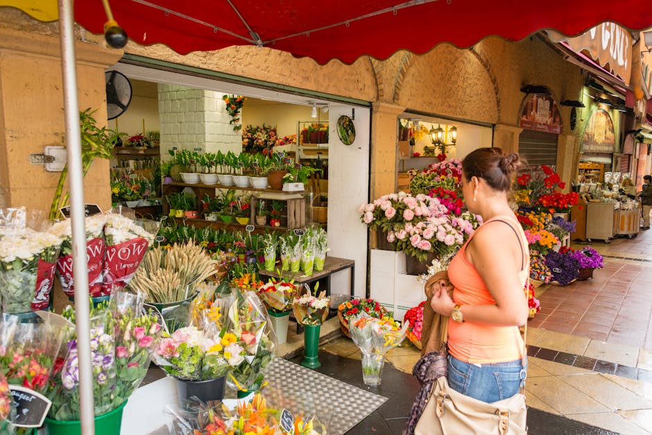 A woman stands outside a flower shop, browsing a vibrant floral display near Clock House station Beckenham. The shop features an array of fresh flowers, including pink and white roses, purple and yell